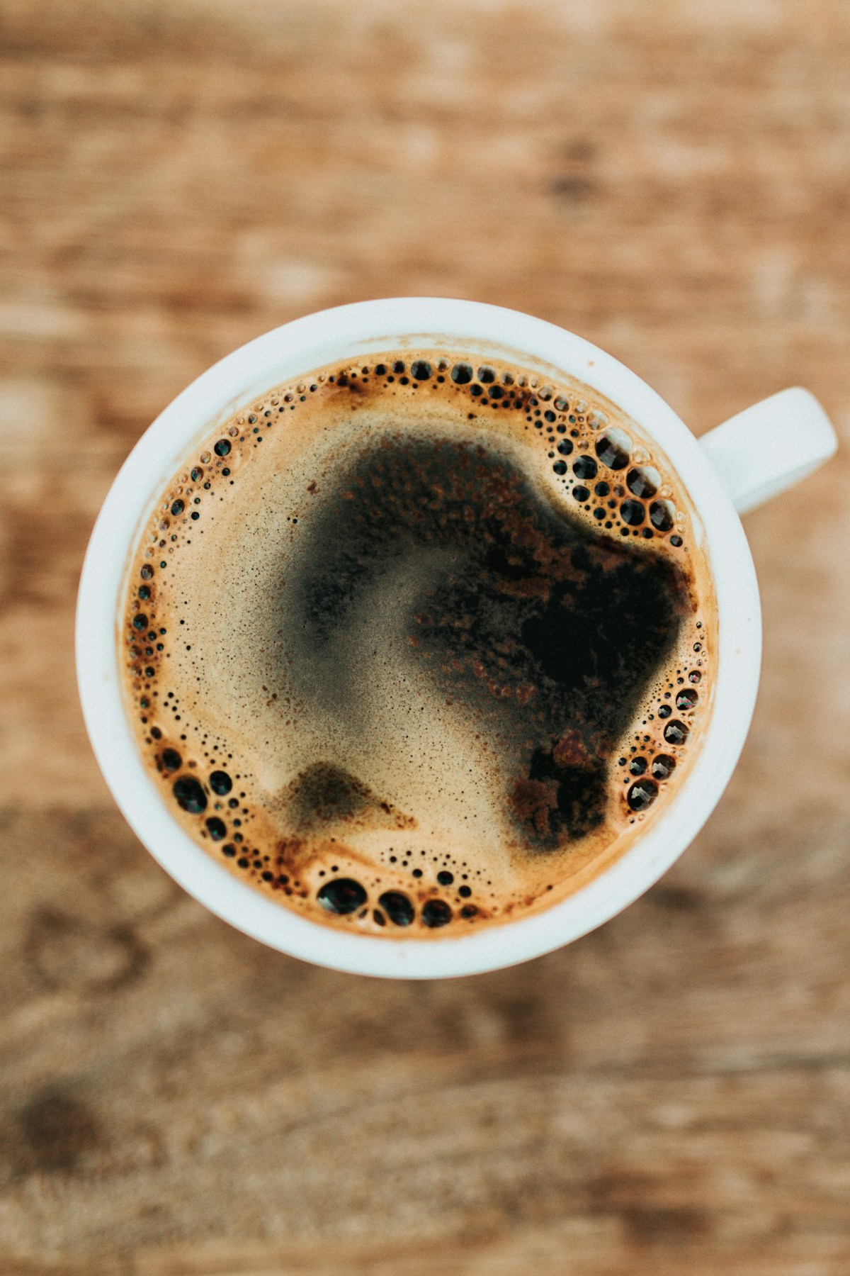 A quiet coffee moment: a white ceramic cup of black coffee on a warm wooden table